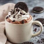 A creamy and chocolatey Oreo mug cake recipe topped with whipped cream, crushed Oreo cookies, and a whole Oreo biscuit, served in a rustic ceramic mug. A quick and easy dessert made in minutes.