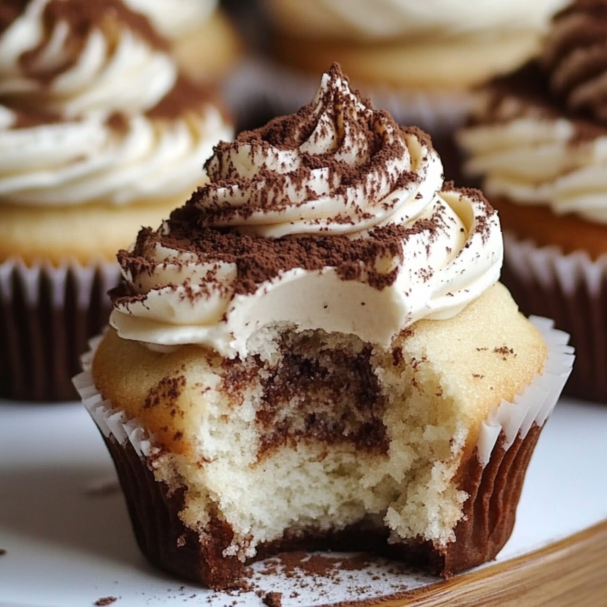 Homemade tiramisu cupcakes with mascarpone frosting and cocoa dusting, bitten to reveal a soft, coffee-soaked center.