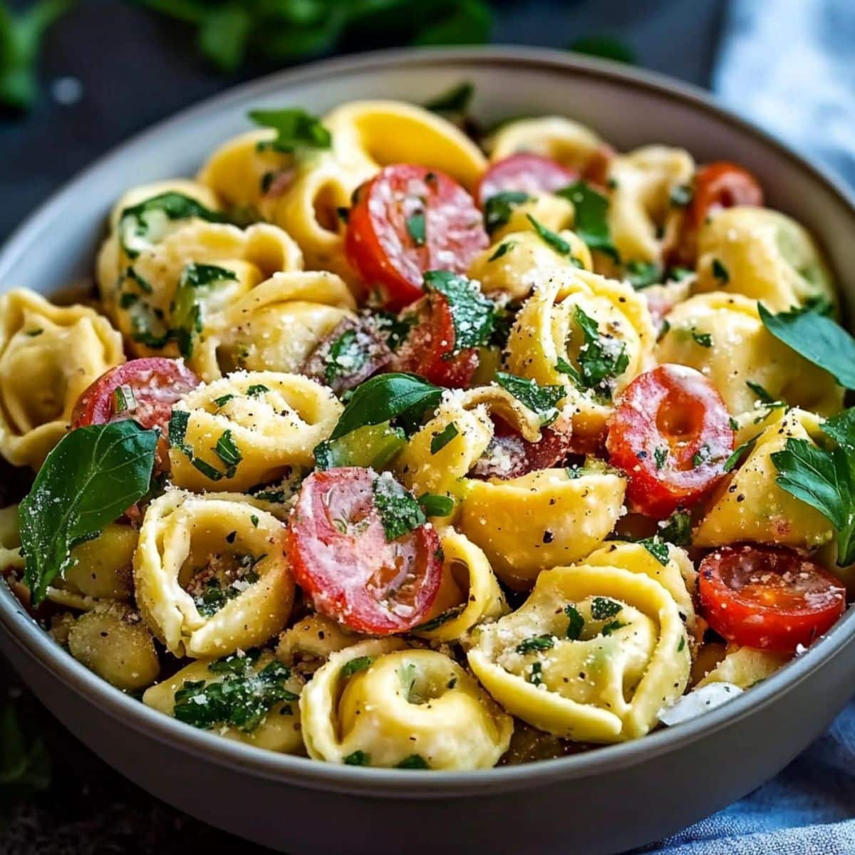 Homemade tortellini pasta salad with cheese tortellini, cherry tomatoes, fresh herbs, and grated Parmesan in a ceramic bowl.