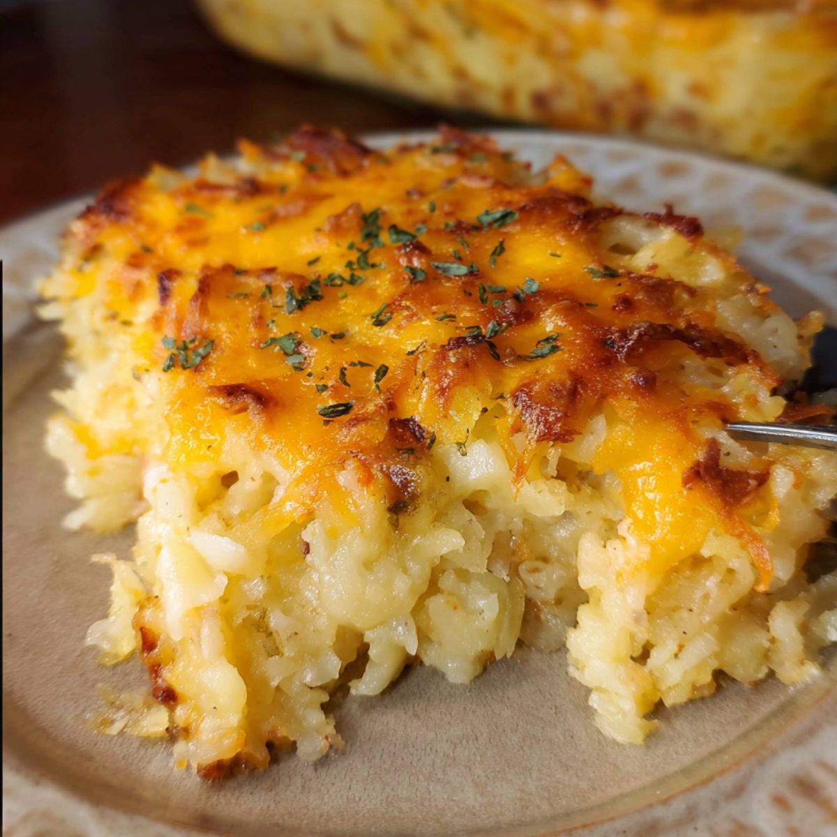 Slice of homemade hashbrown casserole with a crispy cheesy top and creamy potato center, garnished with parsley on a ceramic plate.