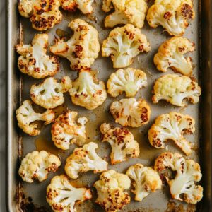 Golden roasted cauliflower florets on a baking sheet, lightly browned and crisped on the edges, ready for the next step in a homemade buffalo cauliflower recipe.
