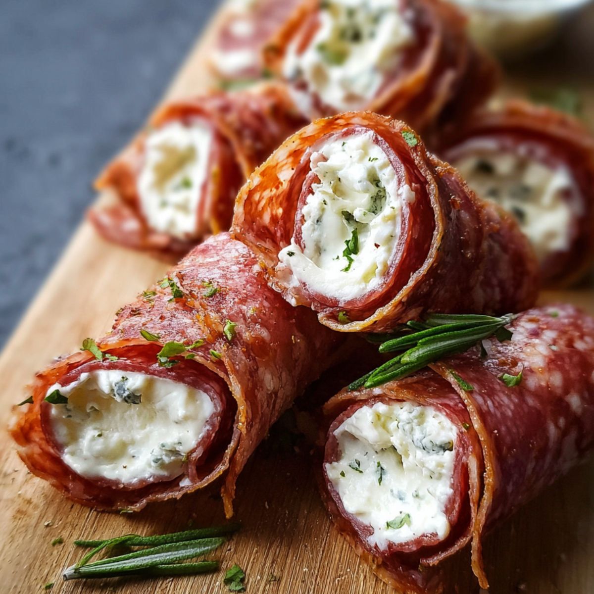 Salami cream cheese roll ups sliced into spirals on a wooden board, filled with creamy cheese and sprinkled with herbs.