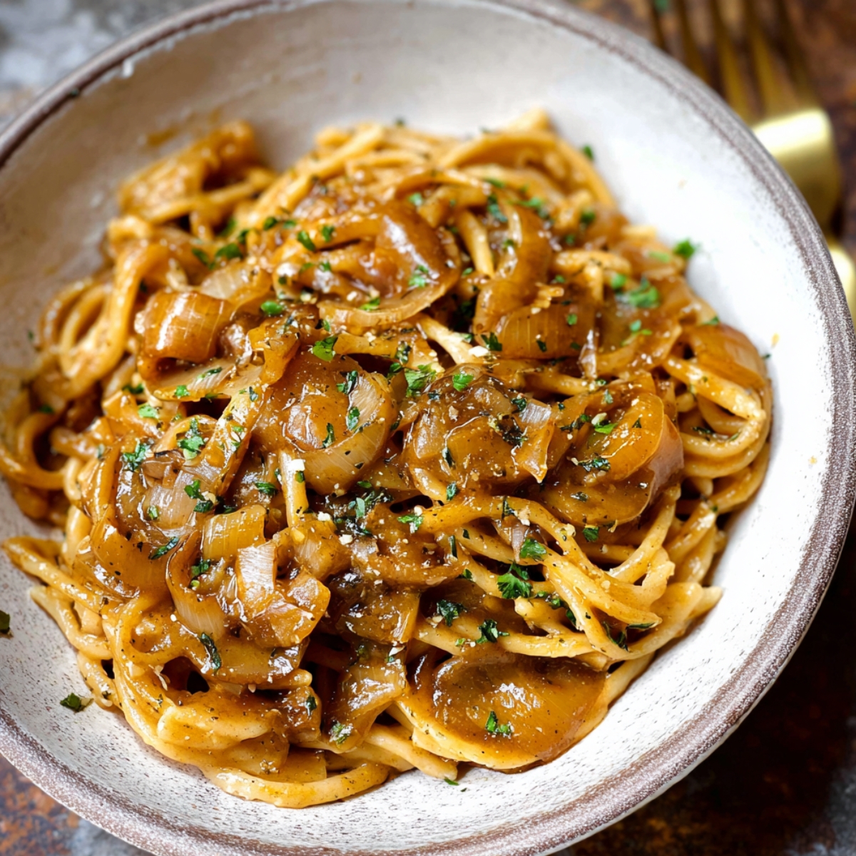 Close-up of homemade French onion pasta in a rustic bowl, topped with caramelized onions and fresh parsley, coated in rich golden sauce.