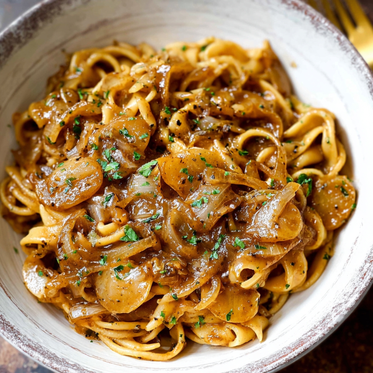 Homemade French Onion Pasta coated in caramelized onion sauce, topped with parsley, served in a rustic ceramic bowl with a fork.