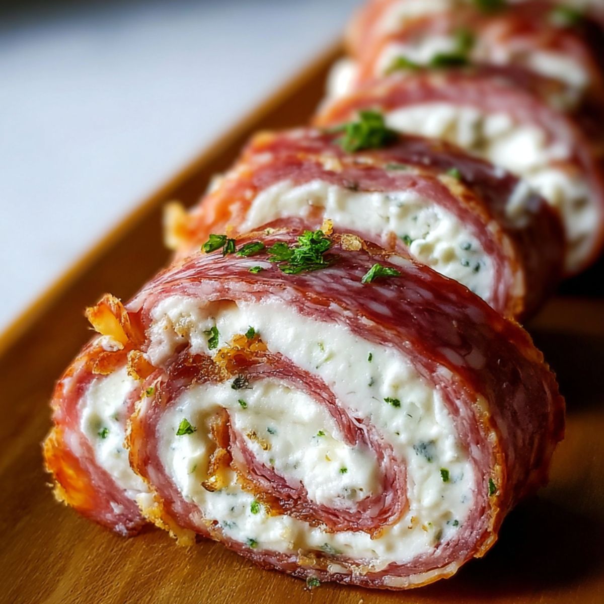 Salami Cream Cheese Roll Ups filled with cream cheese and herbs, sliced on a wooden board with rosemary garnish.