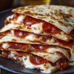 "Close-up of stacked pepperoni pizza quesadillas with melted cheese oozing out, garnished with chopped herbs on a black plate."