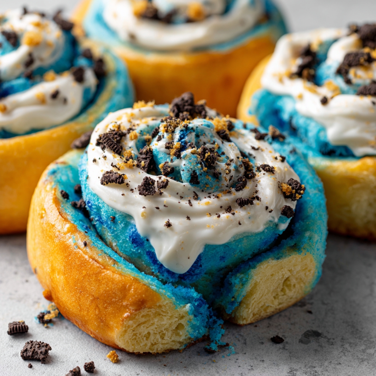 Homemade Cookie Monster cinnamon rolls with golden edges, blue swirled dough, cream cheese frosting, and Oreo crumbles.