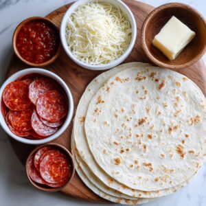 "Top-down view of ingredients for pepperoni pizza quesadillas: flour tortillas, shredded mozzarella cheese, butter, marinara or pizza sauce, and pepperoni slices arranged on a wooden board."