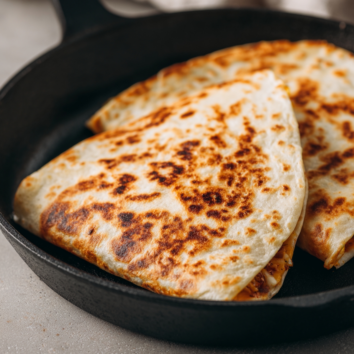 Golden-brown homemade Crunchwrap Supreme in a cast iron skillet, crisp and toasted with melted cheese inside, photographed in soft natural light on a light countertop.