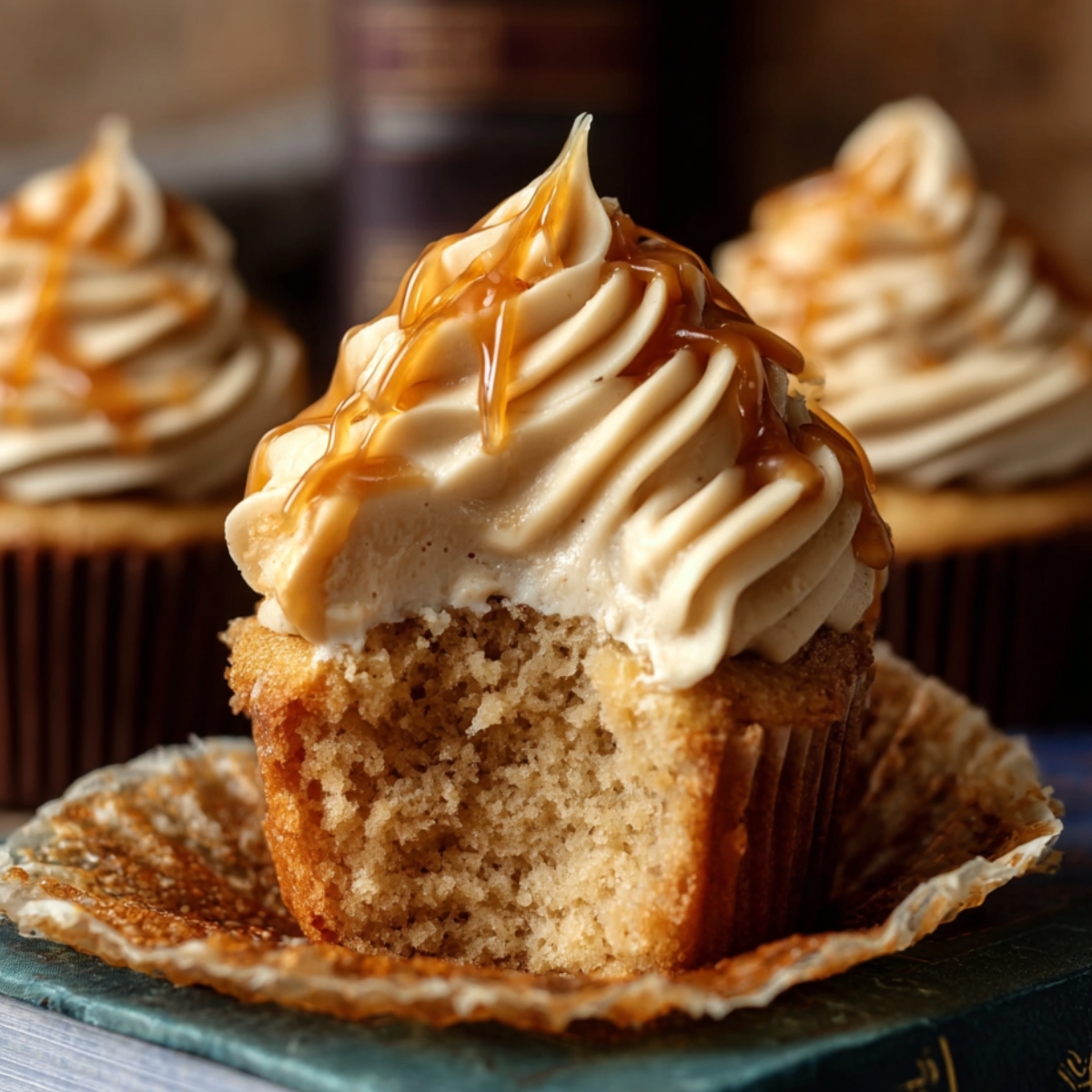 Easy Harry Potter butterbeer cupcakes with caramel-drizzled frosting, one bitten to show soft crumb, sitting on a book with warm, cozy lighting.