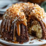 Homemade Samoa Bundt cake drizzled with caramel and topped with toasted coconut on a white plate.