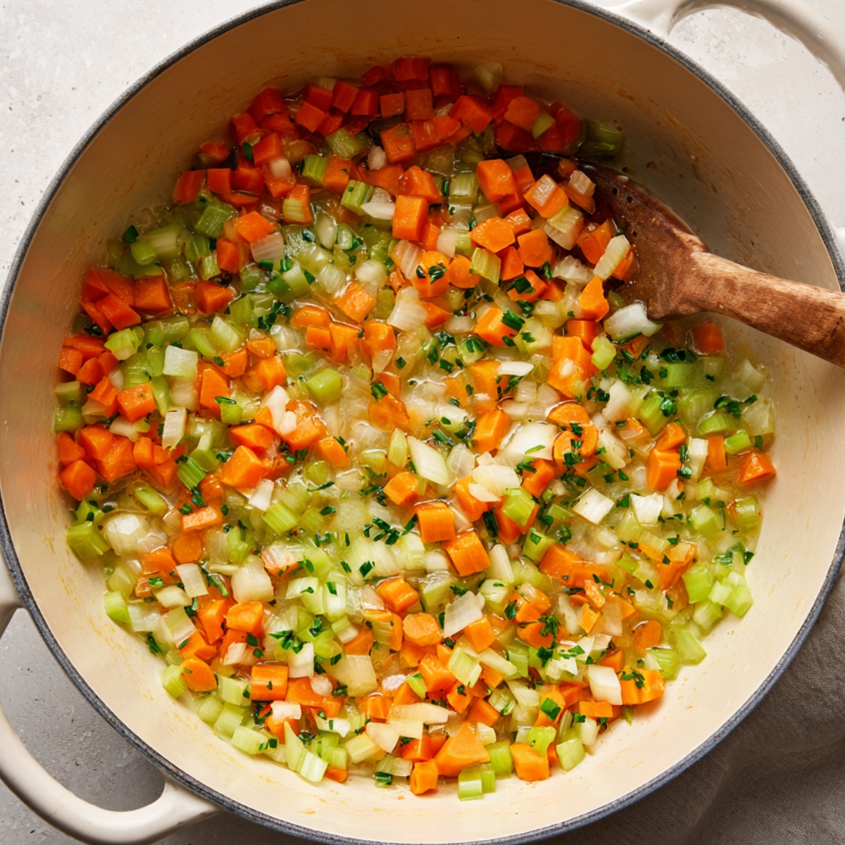 Chopped carrots, celery, and onions sautéing in butter inside a cream-colored Dutch oven, with fresh herbs and a wooden spoon, creating the flavorful base for homemade chicken pot pie pasta.