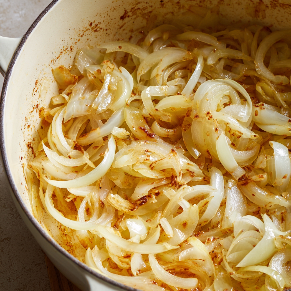 Thinly sliced onions cooking in a Dutch oven, starting to soften and turn golden with light browning around the edges during the caramelization process for homemade French onion pot roast.