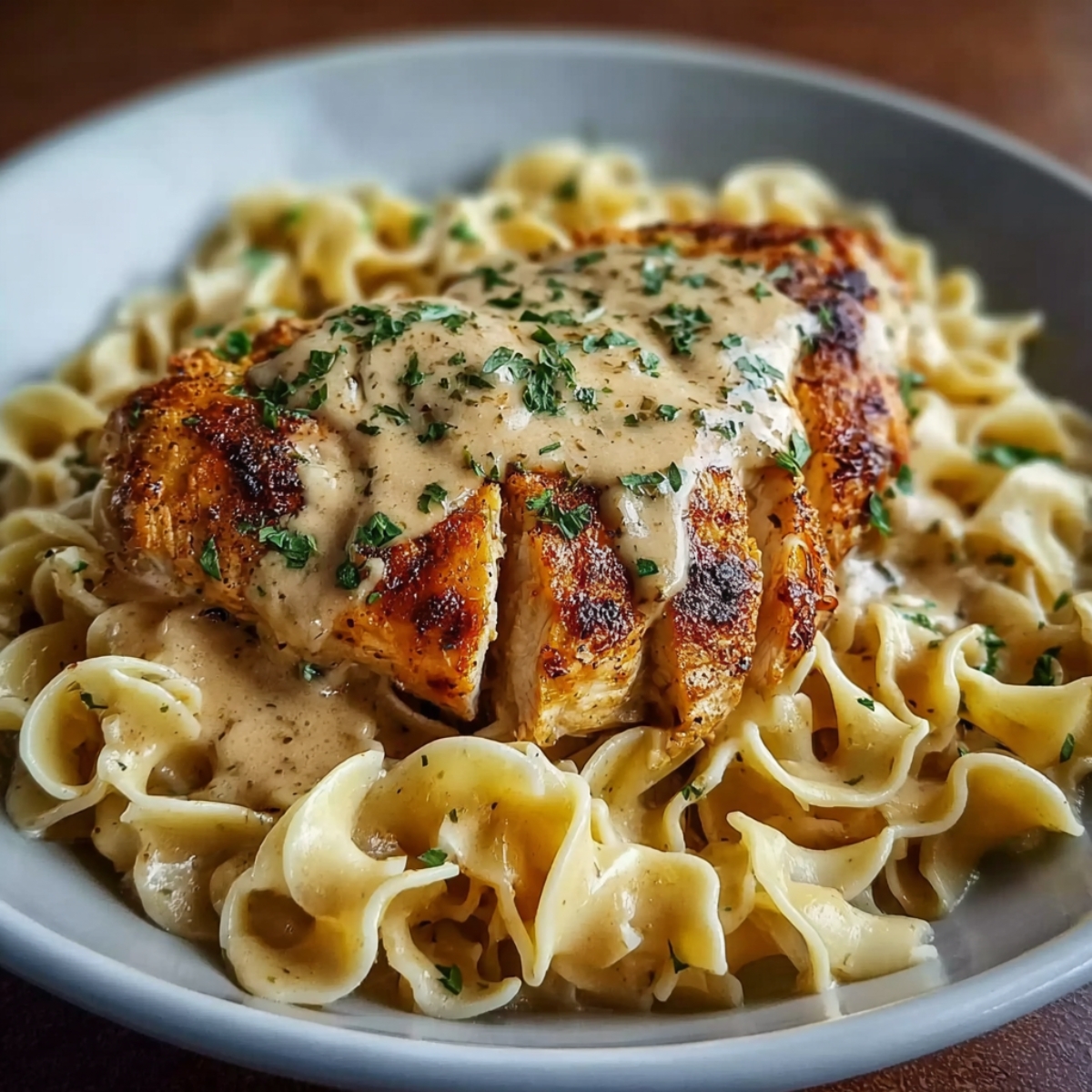 Chicken with Buttered Noodles topped with creamy sauce and parsley, served in a gray bowl.