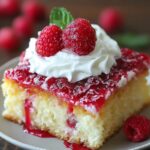 A homemade slice of raspberry zinger poke cake topped with whipped cream, fresh raspberries, and glossy raspberry sauce.