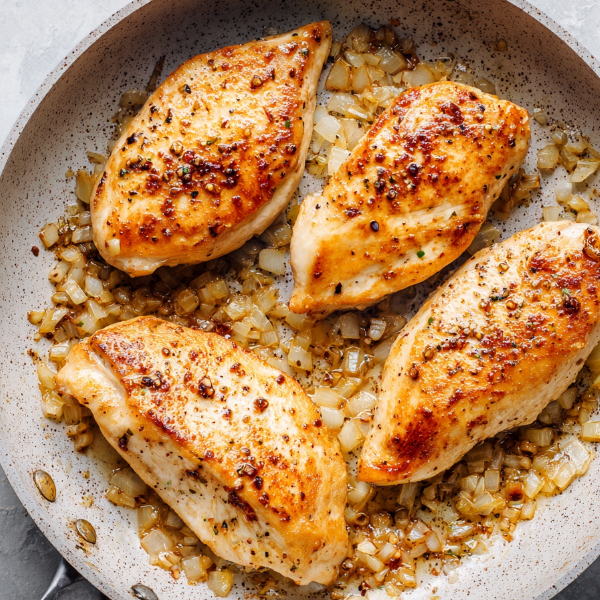 Seasoned chicken breasts searing in a skillet with sautéed onions, cooked until golden and homemade.