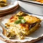 Slice of homemade chile relleno casserole on a rustic plate with melted cheese, roasted chiles, and a forkful taken out.
