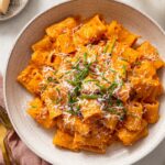 Gochujang Pasta in a creamy orange sauce, topped with grated cheese and fresh green chives, served in a bowl.