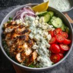 Homemade Greek Chicken Bowls filled with seasoned chicken, tomatoes, cucumbers, red onions, feta, lettuce, and tzatziki.