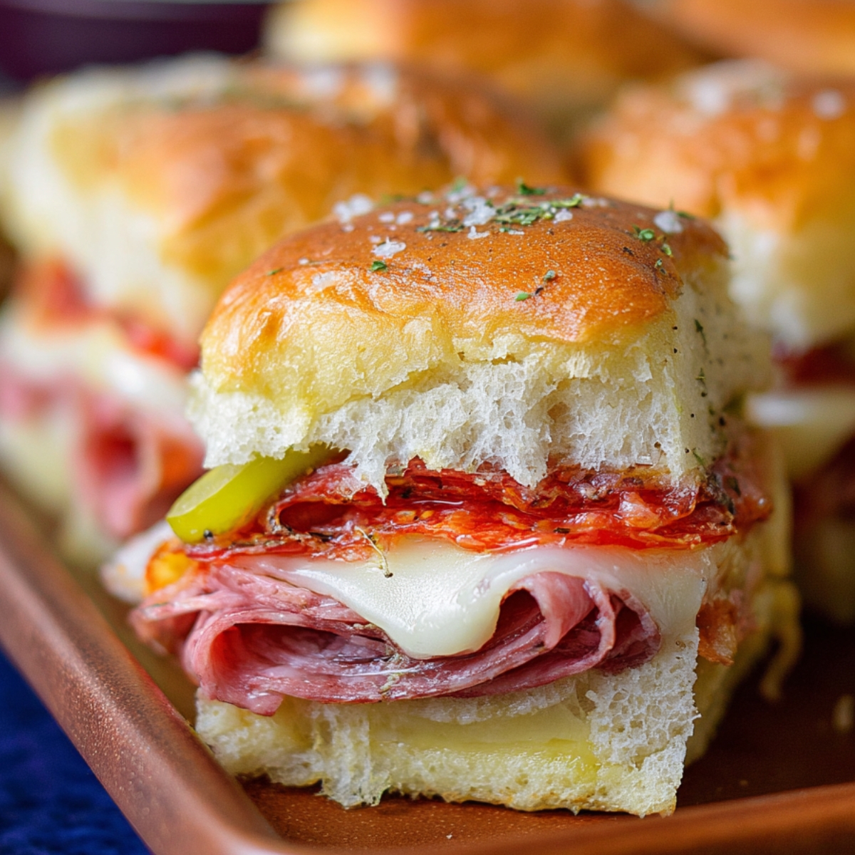 Homemade Hot Italian Sub Sliders with melted cheese, layered deli meats, pepper slices, and a buttery golden roll topped with herbs.