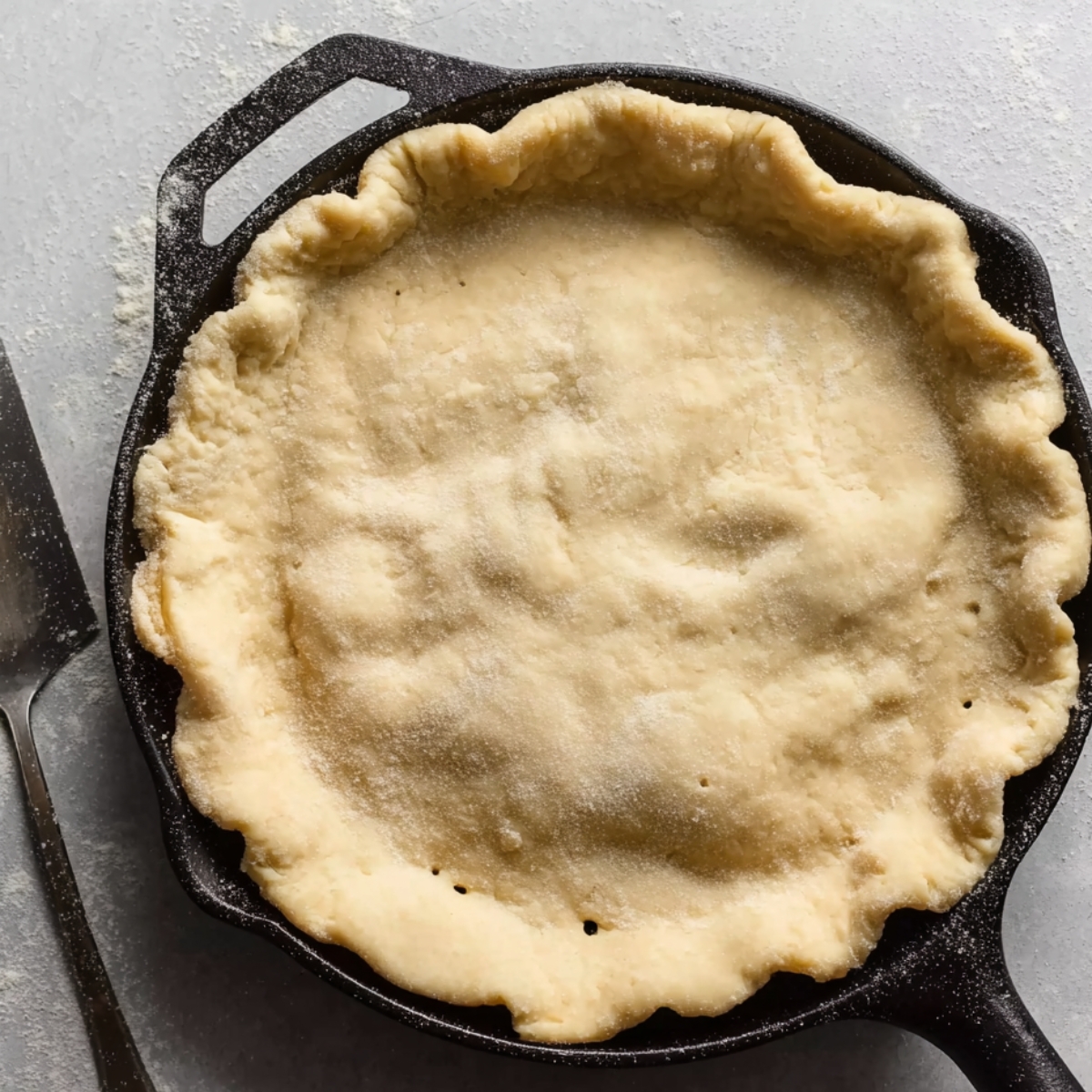 Unbaked pie crust pressed into a cast iron skillet, fluted edges and docked with fork holes, ready for pear tarte tatin.
