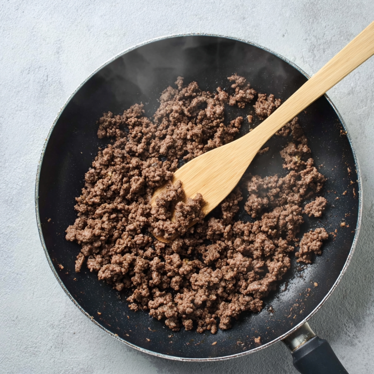 Pan-frying ground beef in a black skillet for cheeseburger quesadillas.