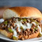 A close-up of a Philly Cheesesteak Sloppy Joes sandwich with melted cheese and a savory beef mixture.