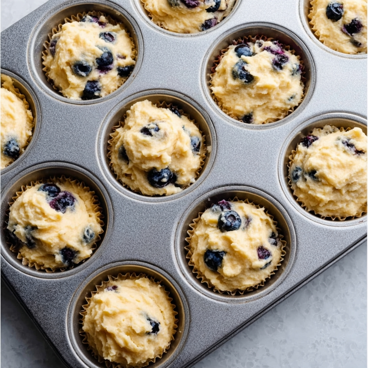 Blueberry muffin batter scooped into lined muffin tin cups before baking
