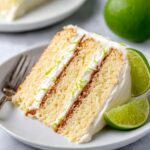 A slice of key lime cake on a plate, garnished with lime slices and frosting.