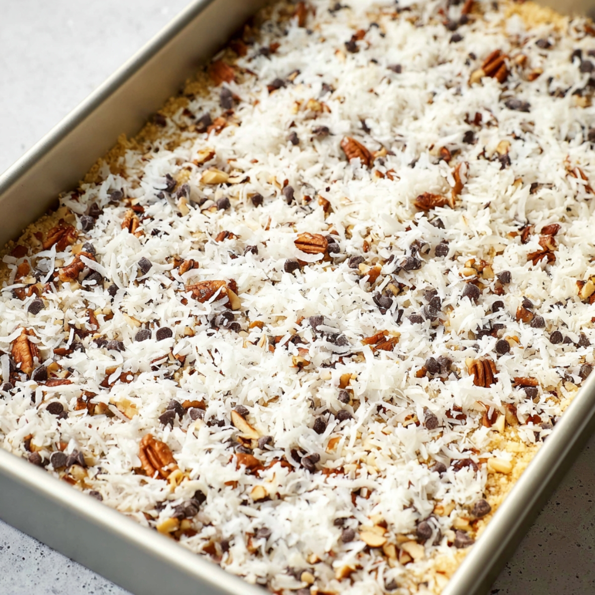 Sprinkle the chocolate chips, butterscotch chips, chopped pecans, and shredded coconut evenly over the crust. Try to distribute them as evenly as you can so every bite gets a little bit of everything.