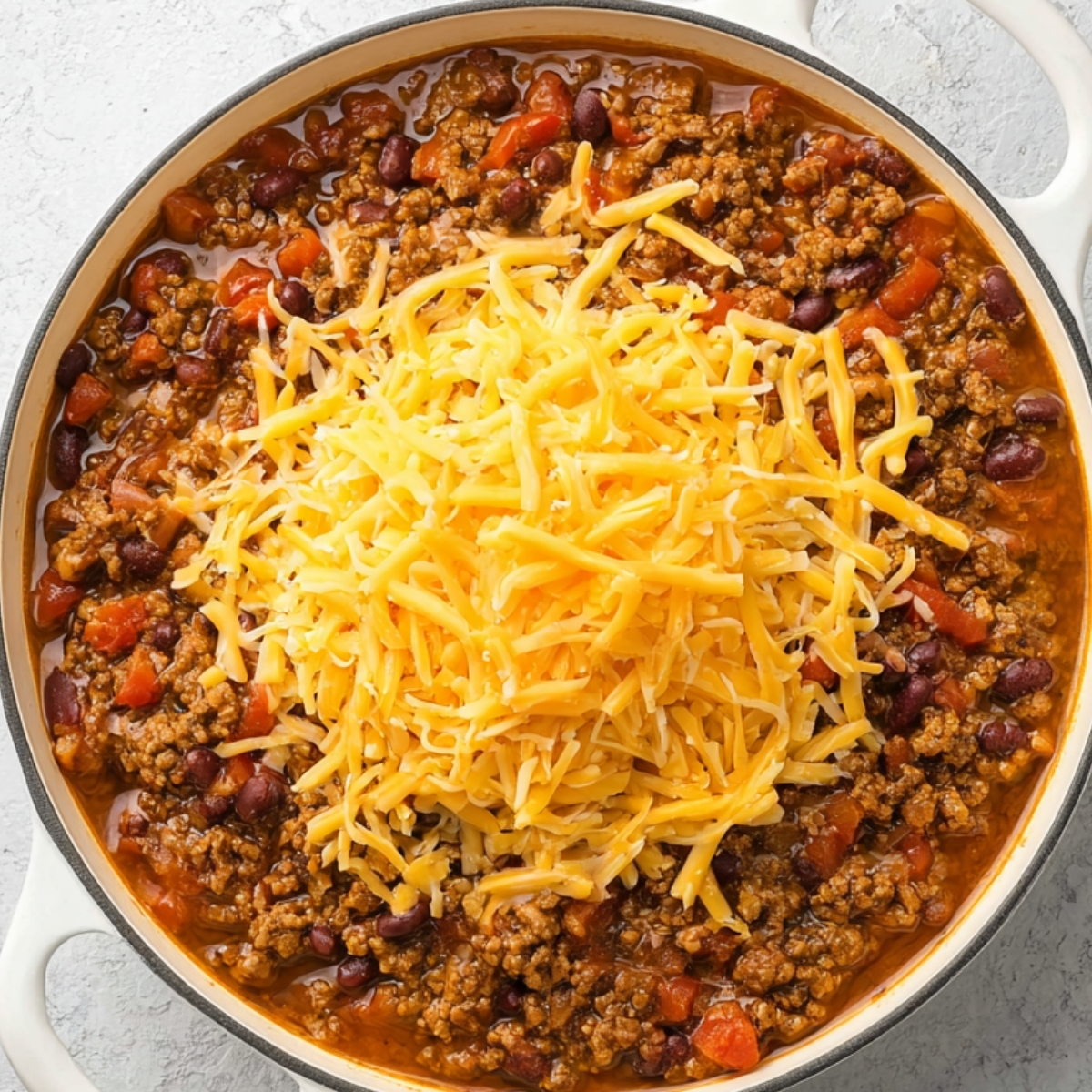 Shredded cheddar cheese melting on top of beef and bean taco casserole in a white skillet, overhead view