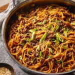 A skillet filled with Mongolian Ground Beef Noodles topped with green onions and sesame seeds, ready to be served.