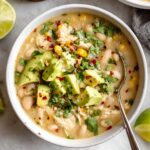 Bowl of white bean chicken chili topped with avocado, cilantro, and red pepper flakes, served with lime on the side.