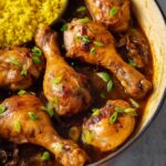 Drizzling sauce over tender Chicken Adobo, served with yellow rice and garnished with fresh herbs.