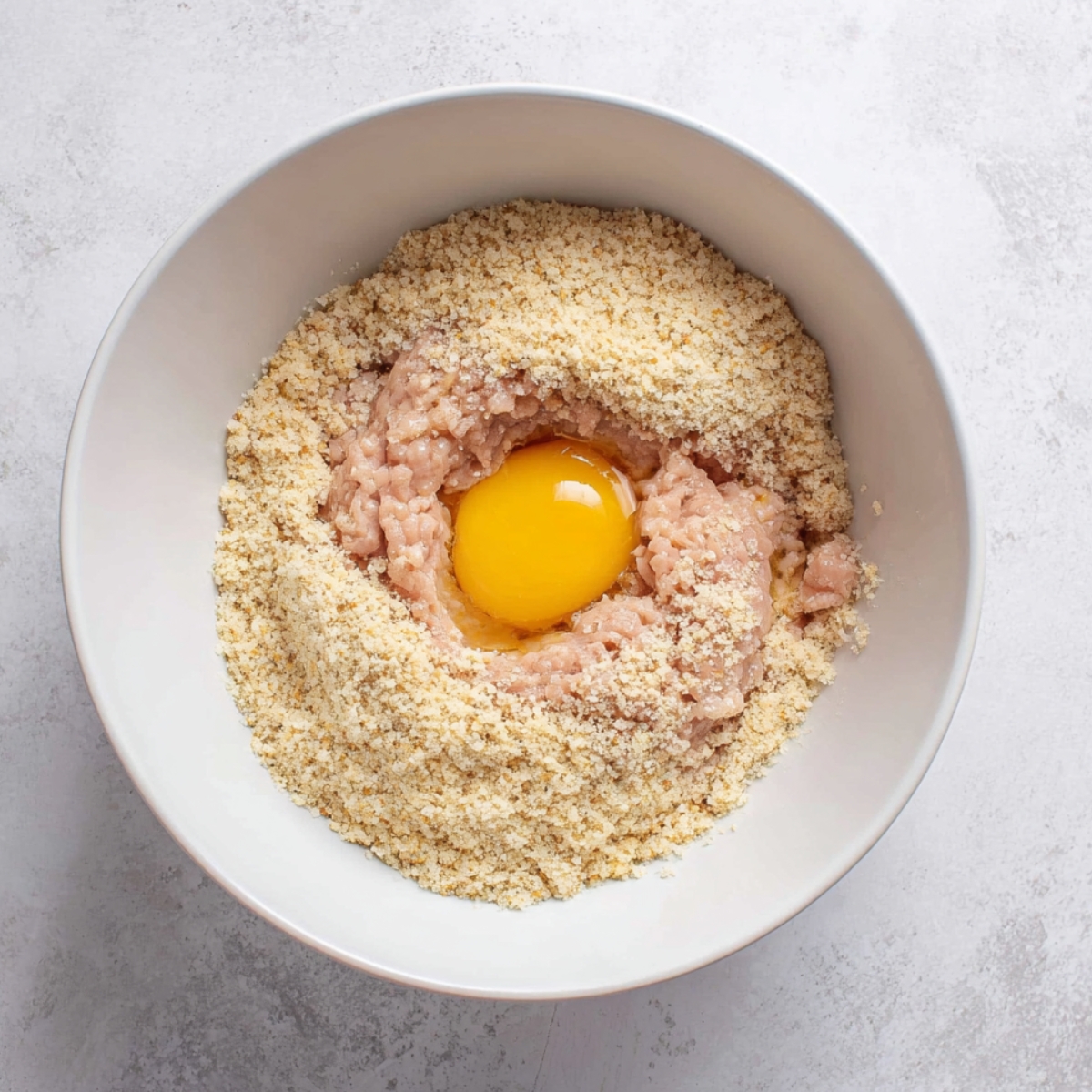 Ground chicken, breadcrumbs, and egg mixture in a white bowl