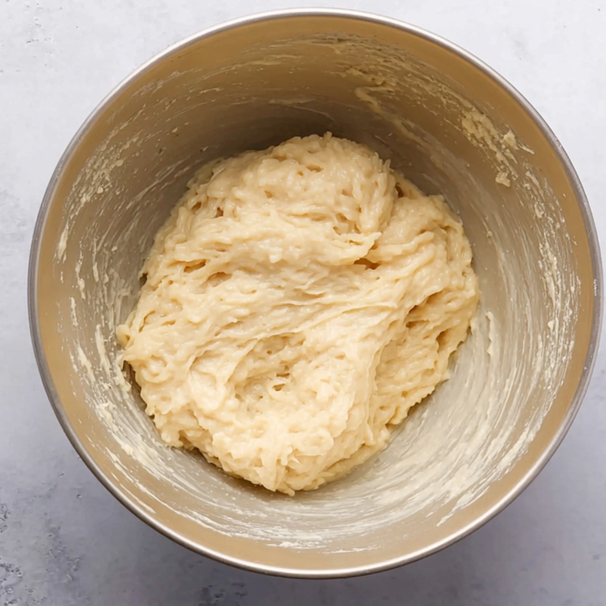 Thick and sticky spaetzle dough in a mixing bowl, ready to be cooked.