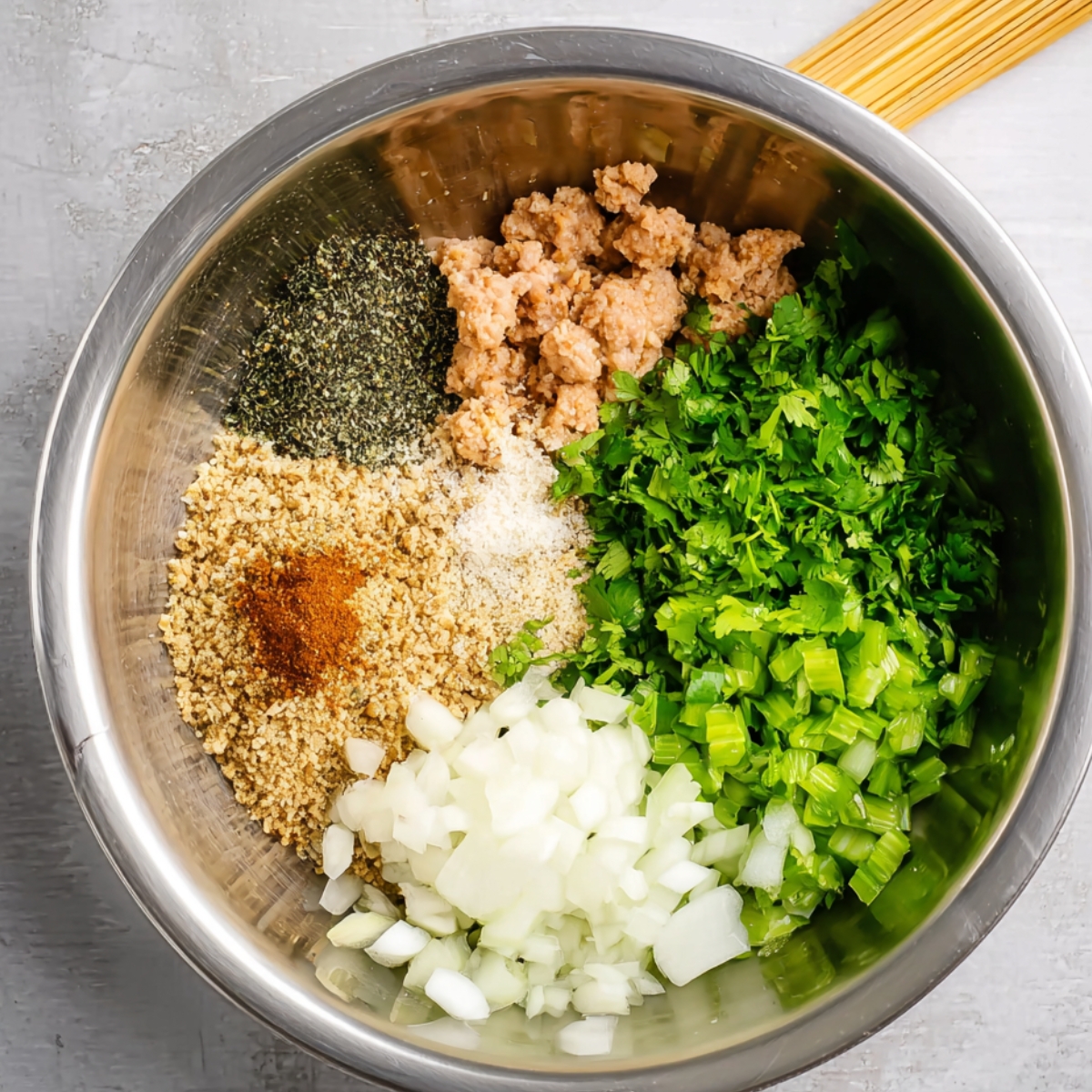 A stainless steel bowl filled with ground chicken, spices, breadcrumbs, cilantro, onions, and other ingredients being mixed to create kofta kebabs.