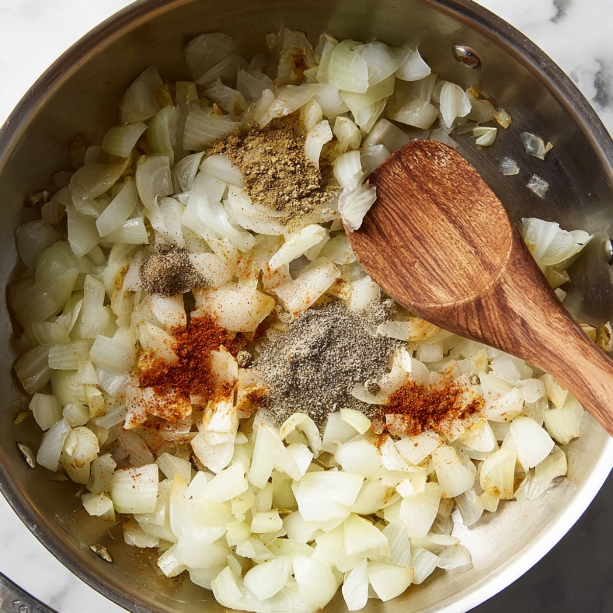 Sautéed onions with various spices including paprika, cumin, and black pepper in a skillet.