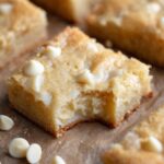 A deliciously baked White Chocolate Brownies with a bite taken out, revealing its soft, gooey texture and scattered white chocolate chips.
