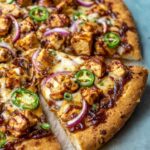 A freshly baked BBQ Chicken Pizza with crispy crust, topped with grilled chicken, red onions, jalapeño slices, and melted cheese.