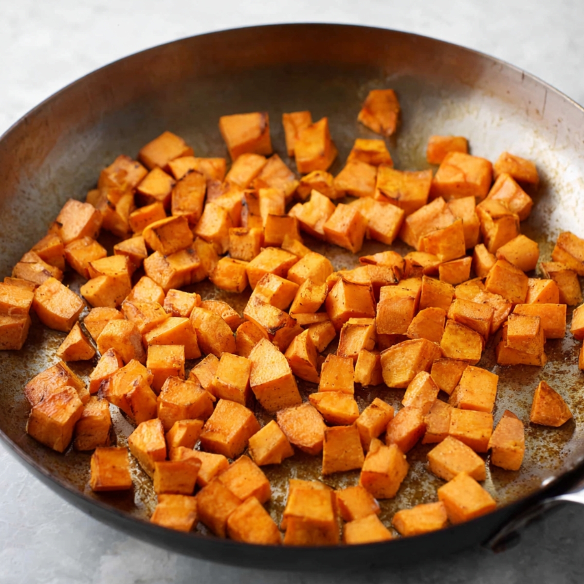 Diced sweet potatoes sautéing in a skillet, lightly browned and crispy on the outside.