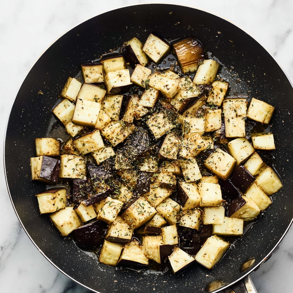 Cubed eggplant seasoned and sautéed in a pan.