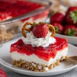 Slice of strawberry pretzel salad topped with whipped cream, strawberry, and pretzel twist.